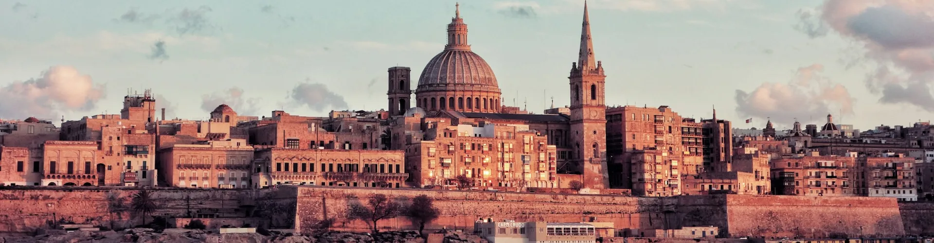 The Valletta skyline at sunset, with the dome of the Carmelite Church above the fortified harbour walls of Malta.